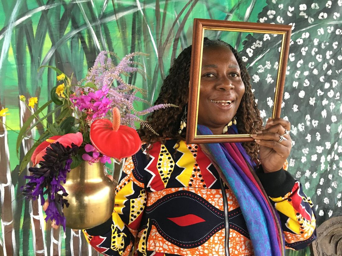 Une invitée tenant un cadre photo près d'un vase doré de fleurs